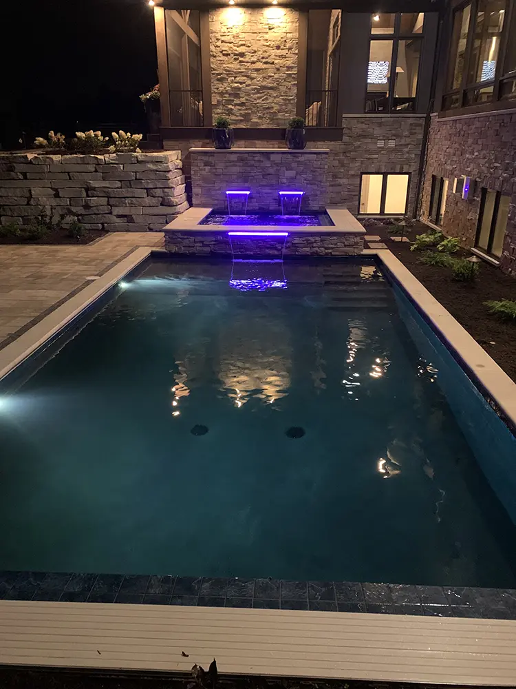 rectangle shaped pool with stone fountain with purple lights at night